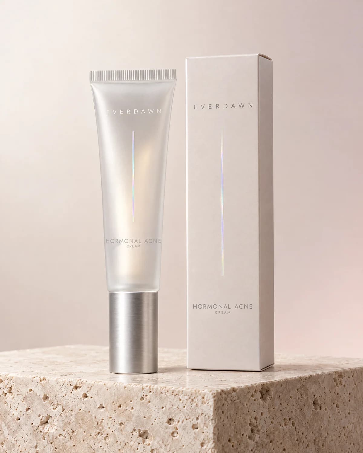 Illustrative packaging: a hormonal acne cream tube beside its carton on a travertine plinth against a soft studio background. Your medicine is labeled and dispensed by the licensed pharmacy.