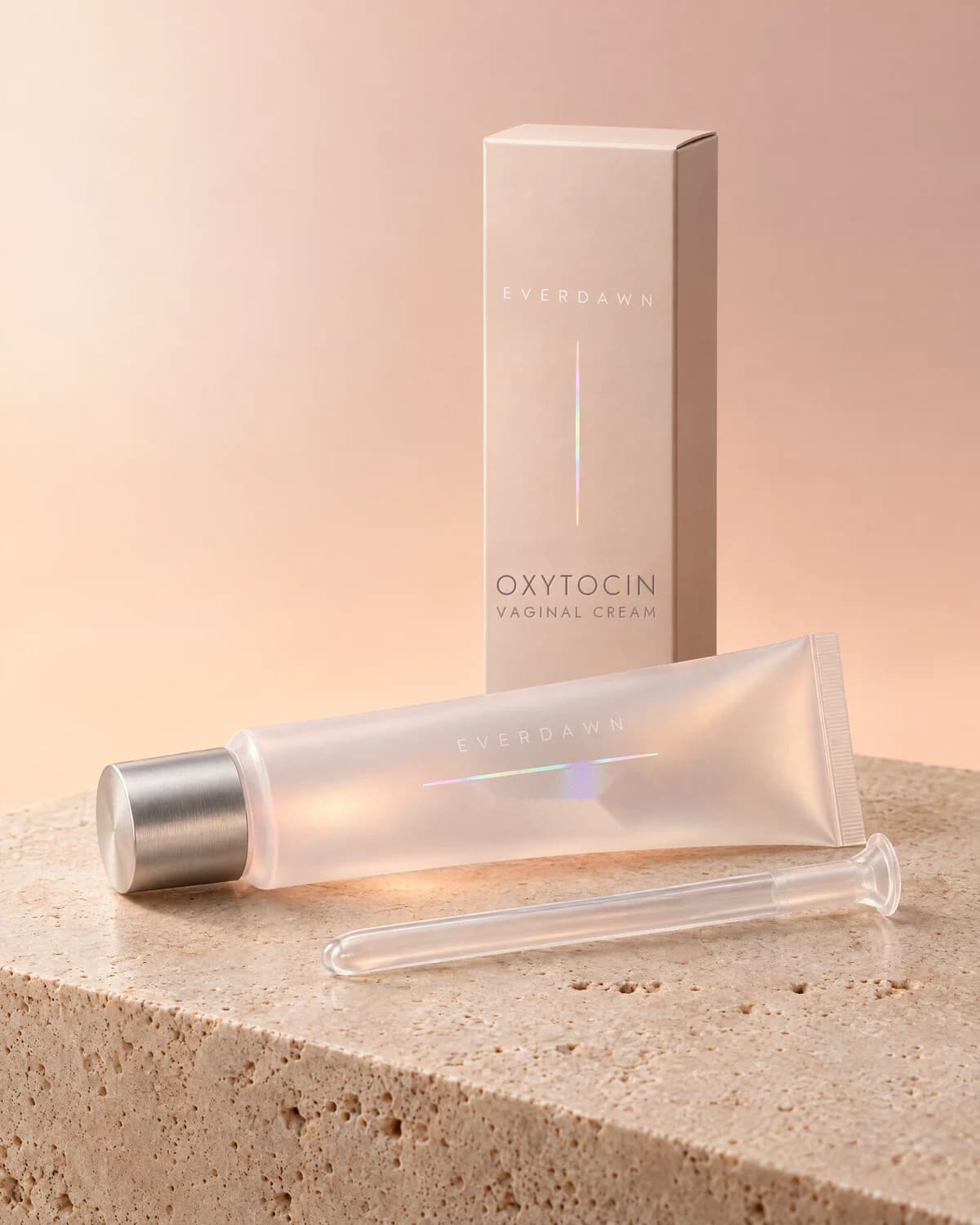 Illustrative packaging: an oxytocin vaginal cream tube with its applicator beside its carton on a travertine plinth against a soft studio background. Your medicine is labeled and dispensed by the licensed pharmacy.